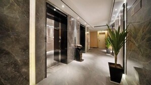 Un pasillo moderno con suelo y paredes de mármol, que incluye una planta en maceta y una puerta con panel de vidrio.
