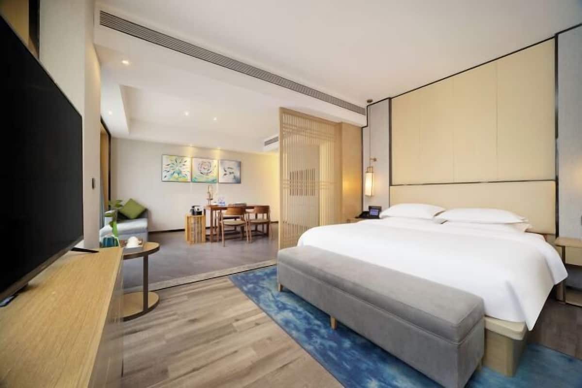 Una habitación de hotel con una cama grande, un escritorio con televisor, una pequeña mesa con sillas y obras de arte en la pared.