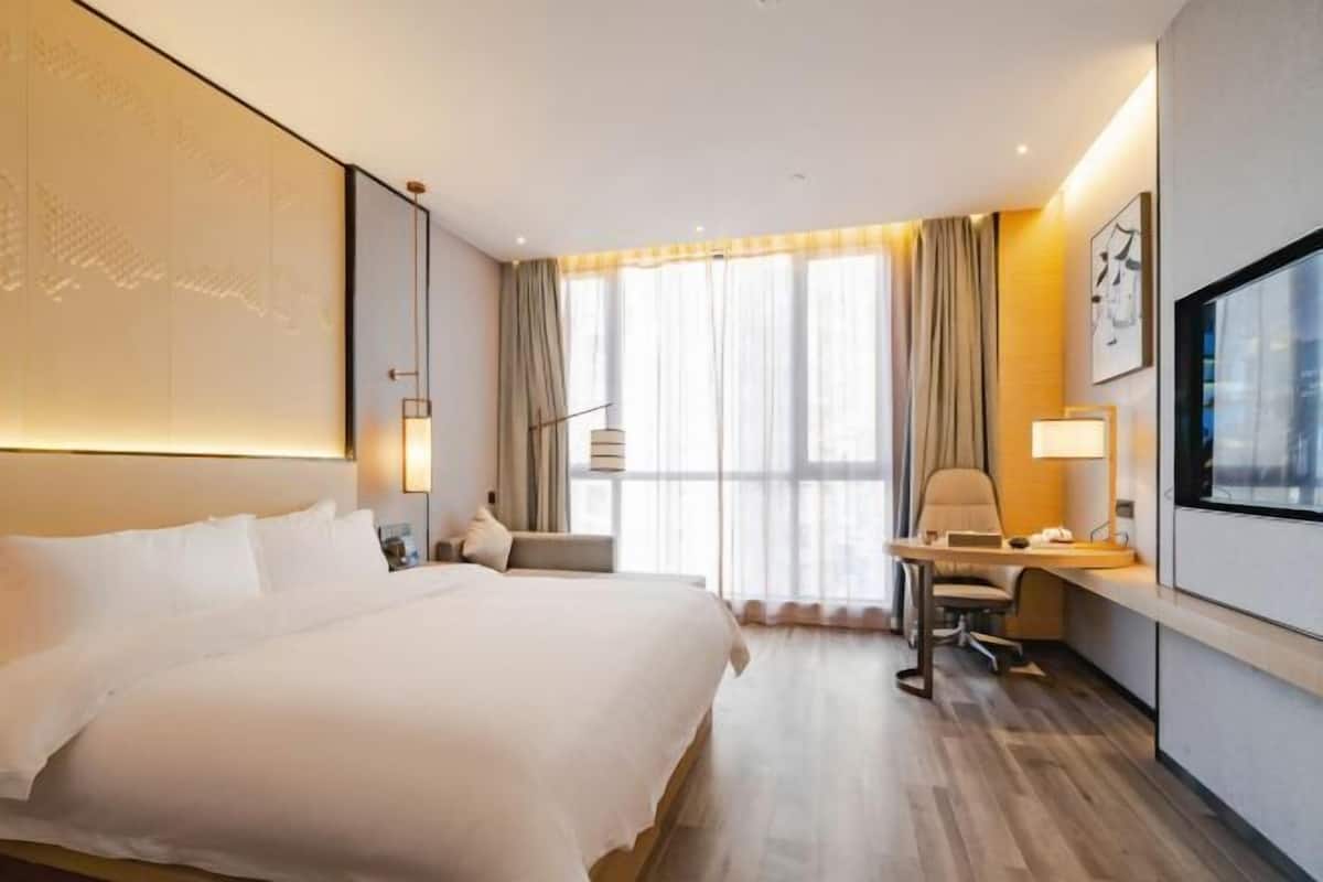 Una habitación de hotel con una cama grande, un escritorio con silla, un televisor y un ventanal con cortinas.