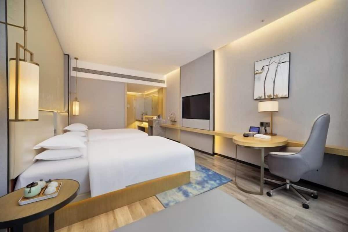 Habitación de hotel con cama, escritorio, silla, televisión y obras de arte.