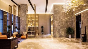 Un amplio vestíbulo con piso de mármol, una zona de estar con sofás, una estantería y un elegante lámpara en el techo.