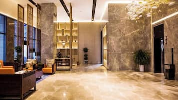 Un amplio vestíbulo con piso de mármol, una zona de estar con sofás, una estantería y un elegante lámpara en el techo.