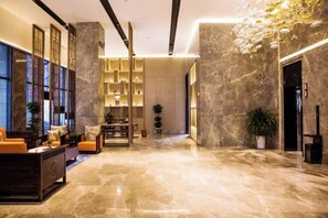 A spacious lobby with a marble floor, a seating area with sofas, a bookshelf, and a decorative ceiling light fixture. - Mandao Hotel (Nanchong)