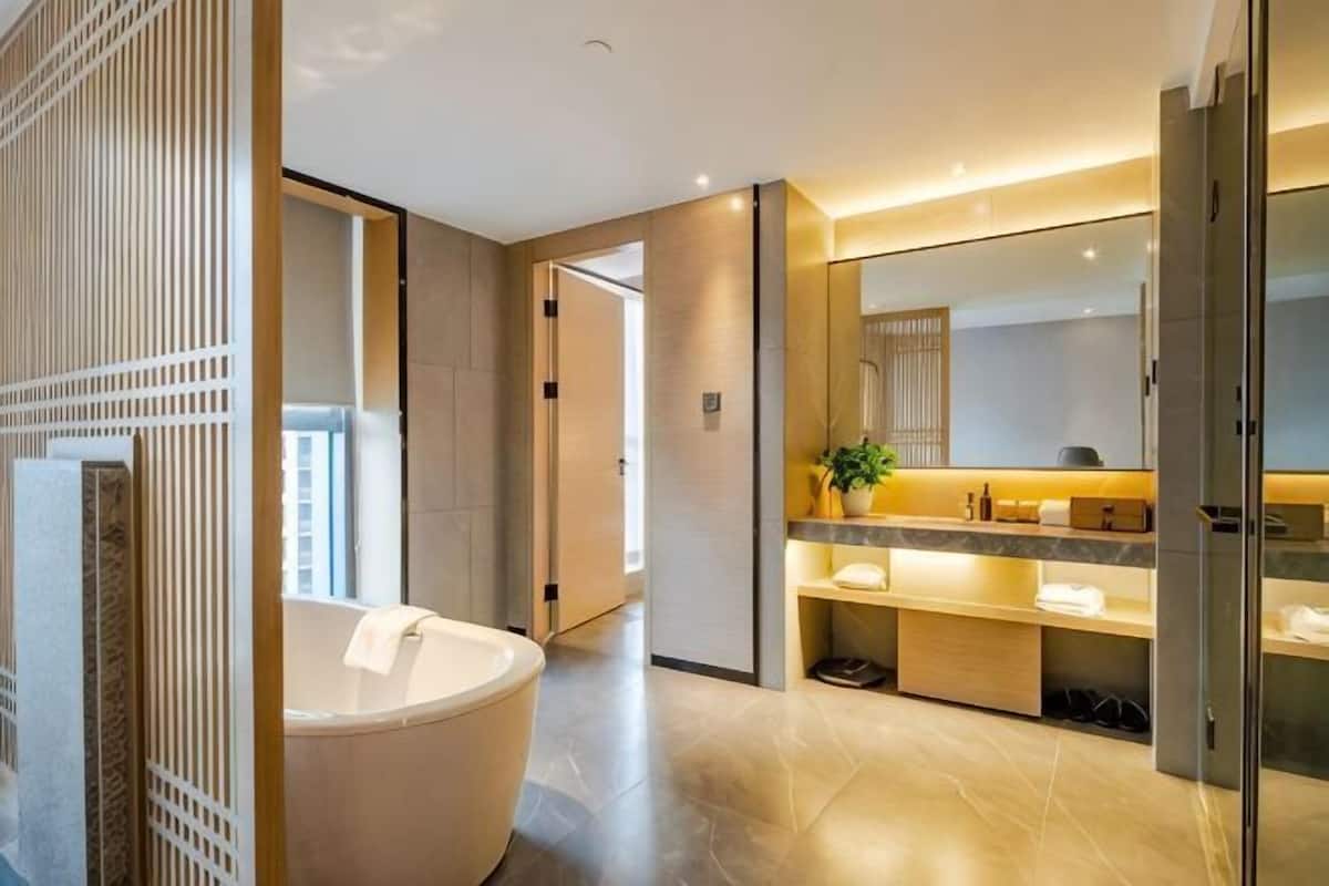 Un baño moderno con una bañera independiente, un espejo grande y un tocador con lavamanos y encimera.