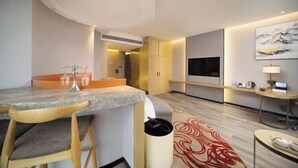 Una habitación de hotel moderna con una mesa de comedor de mármol, sillas de madera, un televisor, un escritorio con computadora y un cuadro grande en la pared.