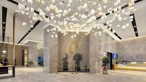 A lobby with a modern design, featuring a marble floor, a reception desk, and a unique ceiling light installation. - Mandao Hotel (Nanbu County)