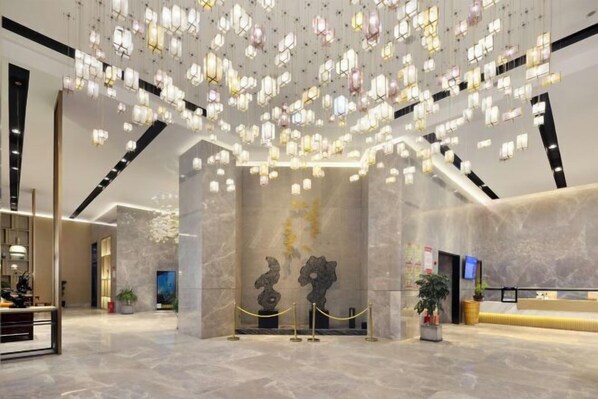 A lobby with a modern design, featuring a marble floor, a reception desk, and a unique ceiling light installation. - Mandao Hotel (Nanchong)