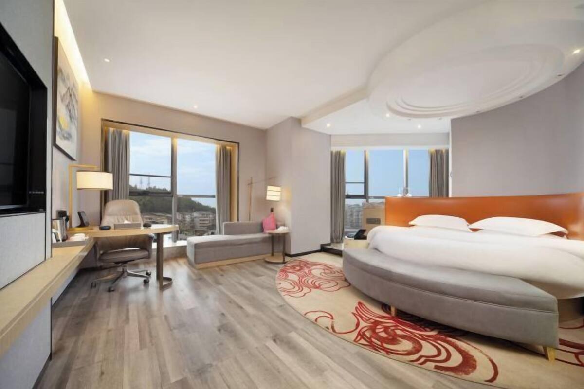 Habitación de hotel con una cama grande, un escritorio, una silla y vistas a la ciudad.