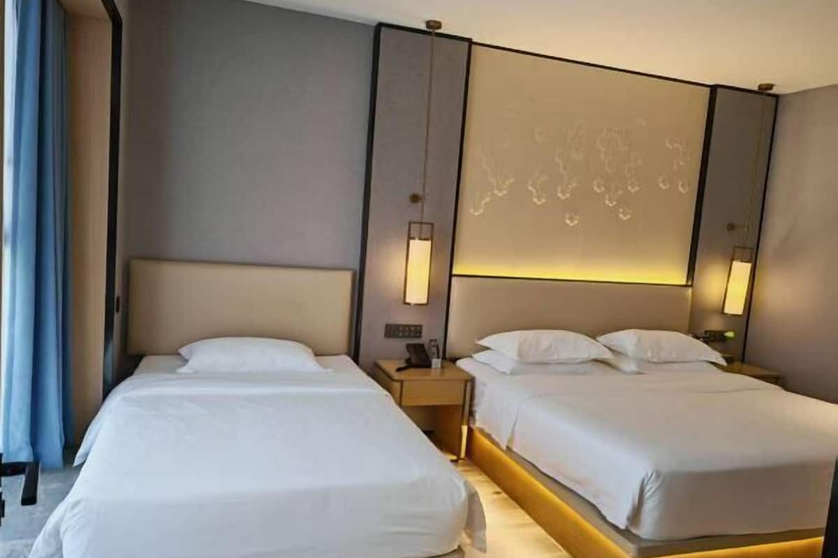 Una habitación de hotel con dos camas, una mesita de noche y una lámpara fijada en la pared.