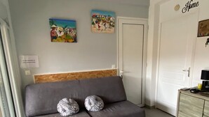 Een woonkamer met een grijze bank, twee gestreepte kussens, een witte salontafel met een bladmotief, en twee decoratieve wandpanelen.