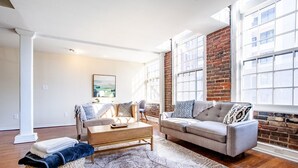 Una sala de estar con sofá, mesa de centro y un ventanal con pared de ladrillo.