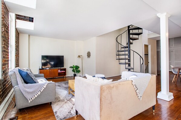 A living room with a TV, two sofas, a coffee table, and a spiral staircase.