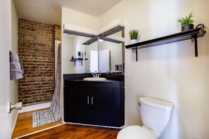 Casa de banho com toucador preto, sanita branca e parede de tijolo.
