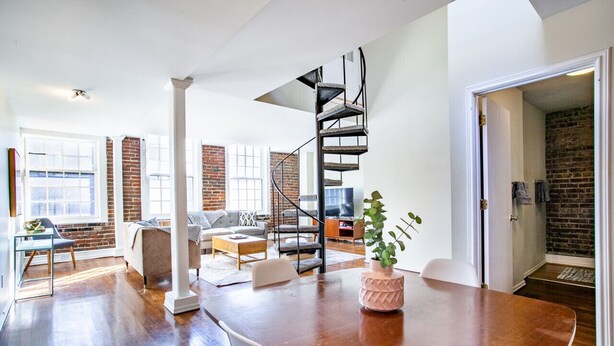Un espacio habitable amplio con piso de madera, una escalera espiral y una pared de ladrillo.
