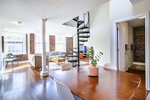 A spacious living area with a wooden floor, a spiral staircase, and a brick wall.