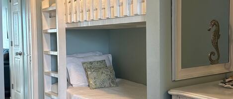 Una cama individual con cabecera, un aparador con detalle de caballito de mar y un espejo en la pared.