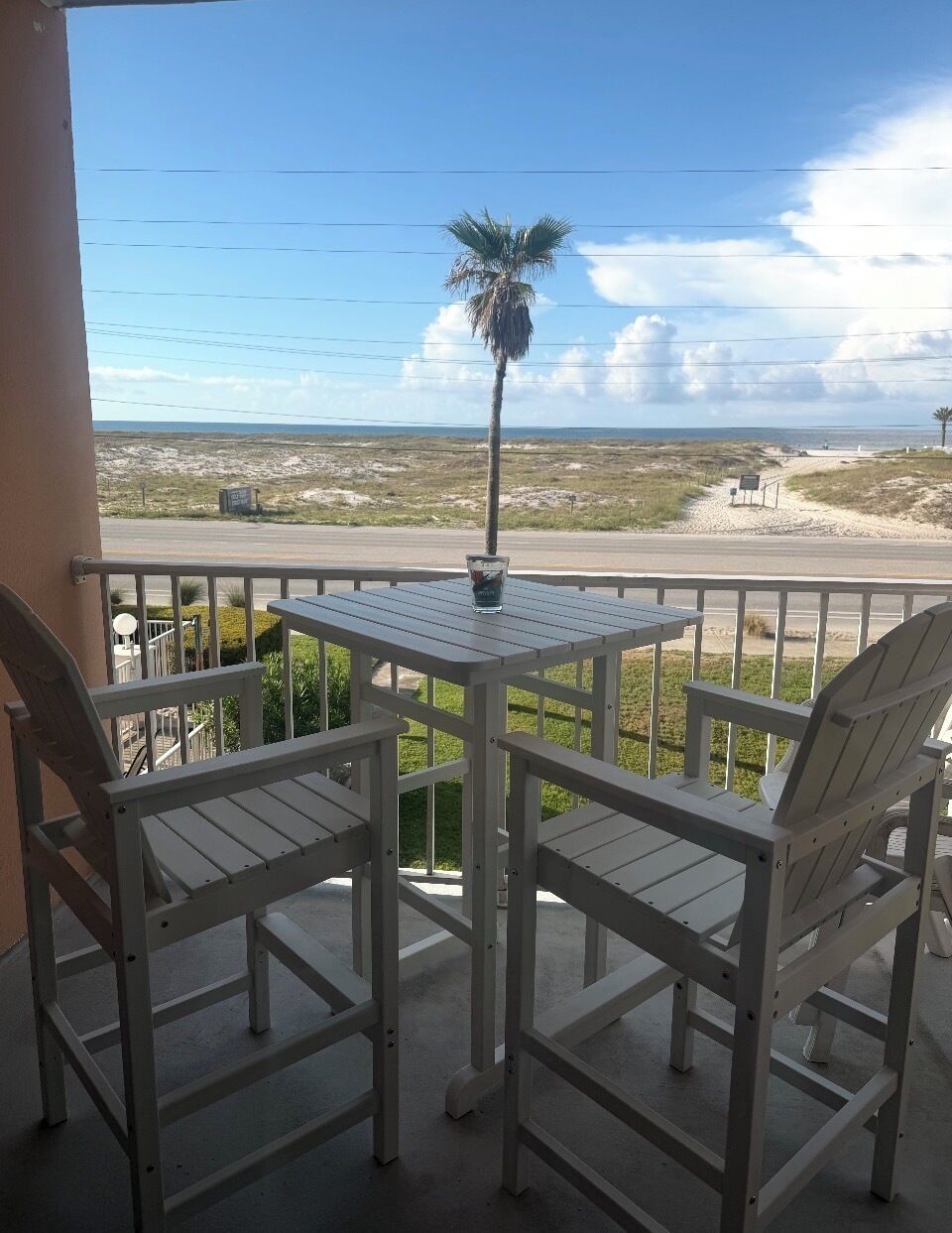 A balcony with a table and chairs, overlooking a beach and dunes.