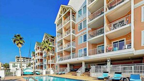 Un hotel de varios pisos con balcones, piscina y sillas de descanso.