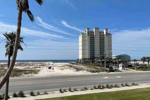 Una carretera costera con un hotel moderno, palmeras y una playa al fondo.