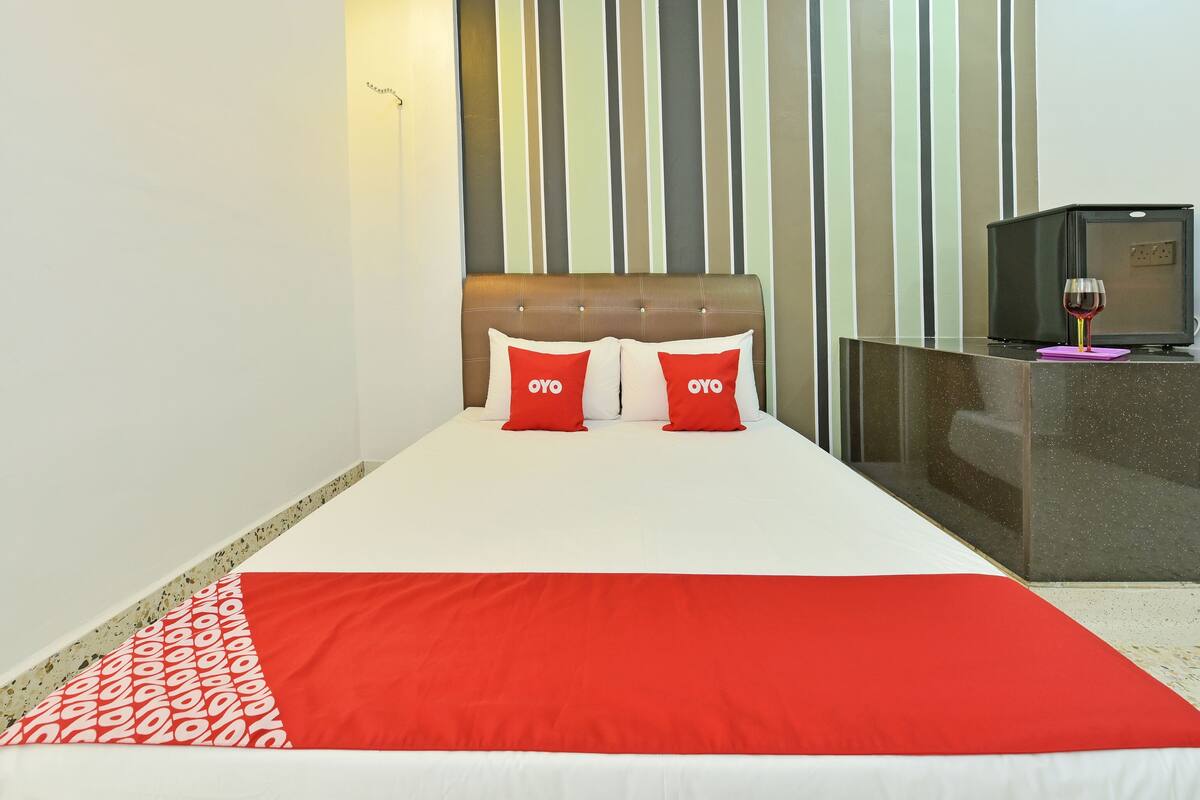 Une chambre d’hôtel avec un lit, deux oreillers rouges ornés du logo « OYO », un téléviseur posé sur un meuble et un mini-bar.