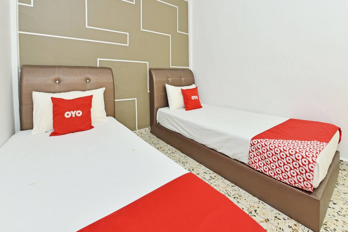 Une chambre d’hôtel avec deux lits, chacun doté d’une tête de lit et d’oreillers, et une couvre-lit rouge et blanche à motifs.