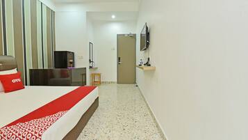 A hotel room with a bed, a desk with a TV, a small table, and a mirror on the wall.