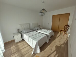 Ein Schlafzimmer mit zwei Betten, Holzboden, einem Kleiderschrank und einem Stuhl.