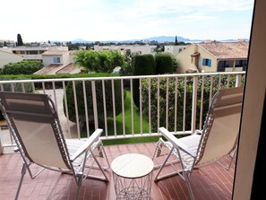 A balcony with two white folding chairs and a small round table.