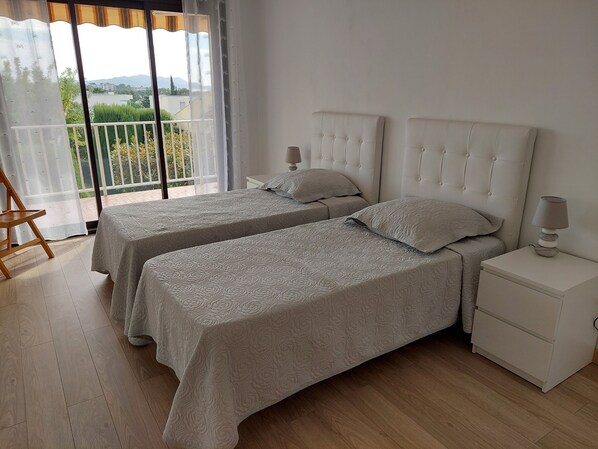A bedroom with two beds, a nightstand, a chair, and a balcony with a view.
