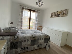 A bedroom with a bed, a chair, a lamp, a radiator, and a window with curtains.