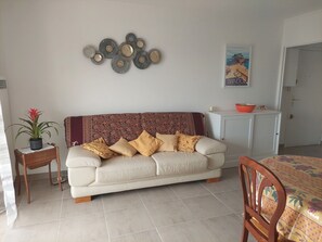 A living room with a sofa, a dining table, a chair, a cabinet, and a decorative wall piece.