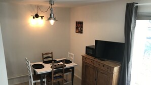 Una cocina compacta con una mesa de comedor, sillas, microondas y televisor sobre un mueble de madera.