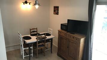 A compact kitchen with a dining table, chairs, a microwave, and a television on a wooden cabinet.