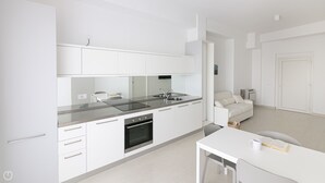 Una cuina moderna amb armaris blancs, taulell d'acer inoxidable i forn de sobre.