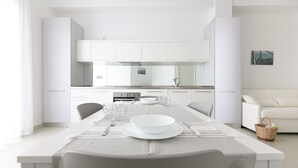 Una cuina moderna amb armaris blancs, una illa central amb seients i una zona de menjador preparada per a quatre.