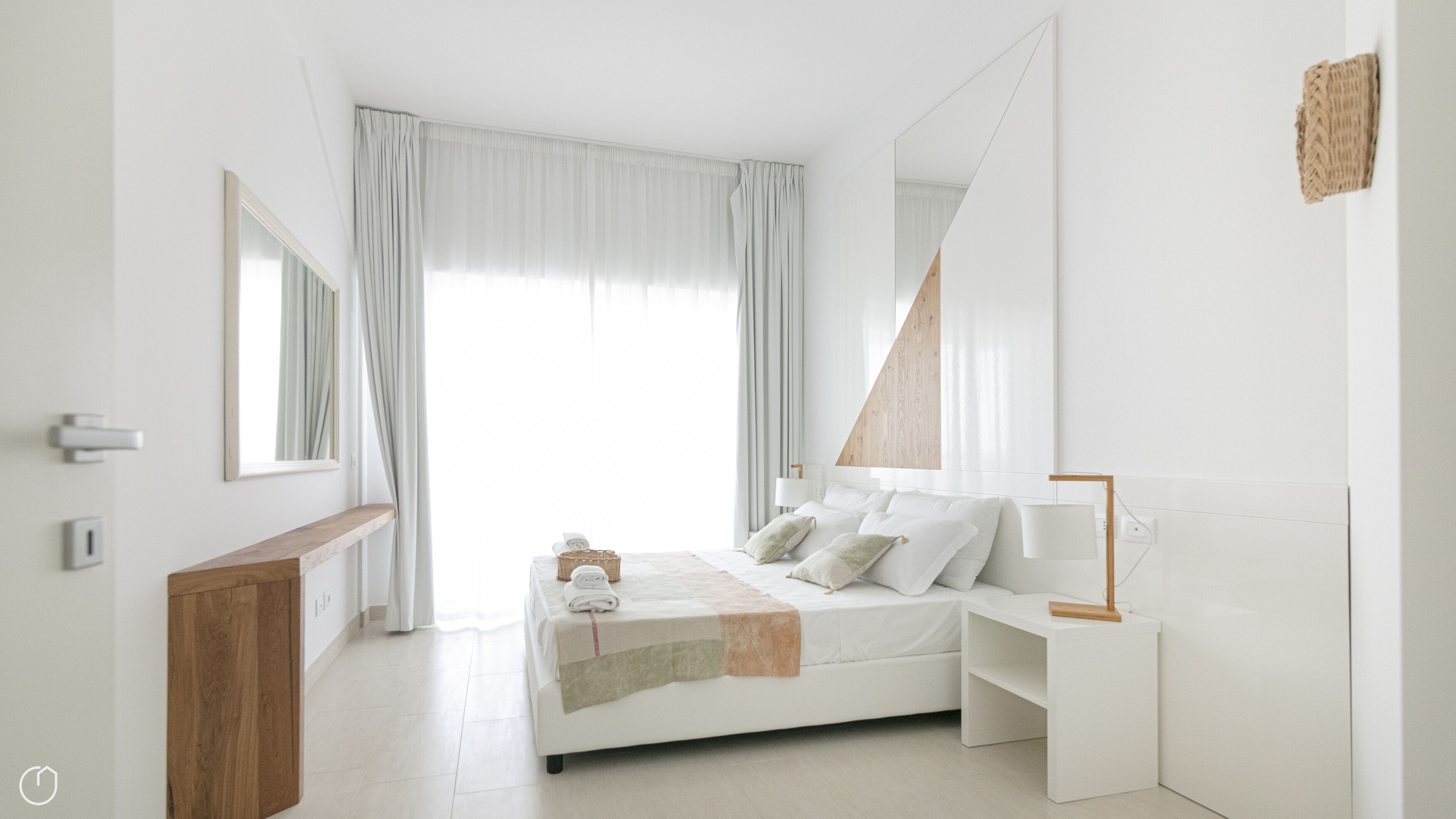 A modern bedroom with a bed, bedside tables, a mirror, and a large window with curtains.