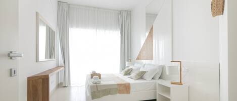 A modern bedroom with a bed, bedside tables, a mirror, and a large window with curtains.