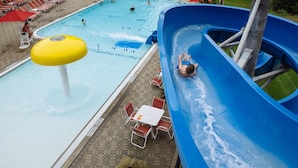 A swimming pool with a water slide, lounge chairs, and a table with chairs.