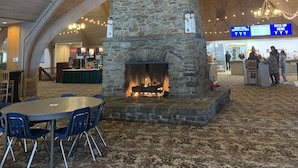 A spacious indoor area with a stone fireplace, wooden ceiling beams, and a patterned carpet.