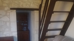 Une pièce avec un mur en pierre, un meuble en bois, un canapé beige et un escalier en bois.