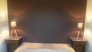 Un lit bien fait, avec une tête de lit, deux tables de chevet avec des lampes et un mur de couleur sombre.