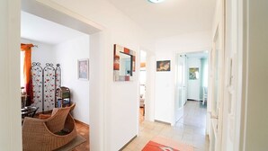Un pasillo con una silla de mimbre, un espejo y un tapete rojo.