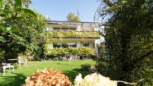 Un edificio con césped verde, vallas blancas y un balcón con plantas.