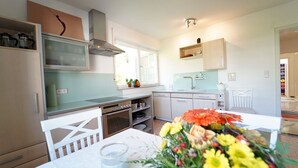 Una cocina moderna con armarios blancos, horno empotrado y comedor con mesa y sillas blancas.