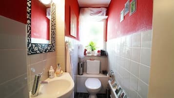 Een kleine badkamer met een wastafel, toilet en een klein raam met een plantje.