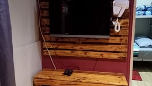 A room with a TV mounted on a wooden panel wall, a bedside phone, a small wooden table with a remote control, and a bunk bed in the background. - OYO Home 90426 Kepayan Dnd Stay (Kota Kinabalu)