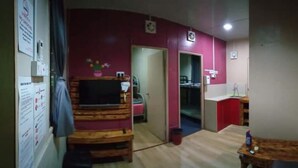 A room with a wooden bed, a small table, a TV, and a red wall. - OYO Home 90426 Kepayan Dnd Stay (Kota Kinabalu)