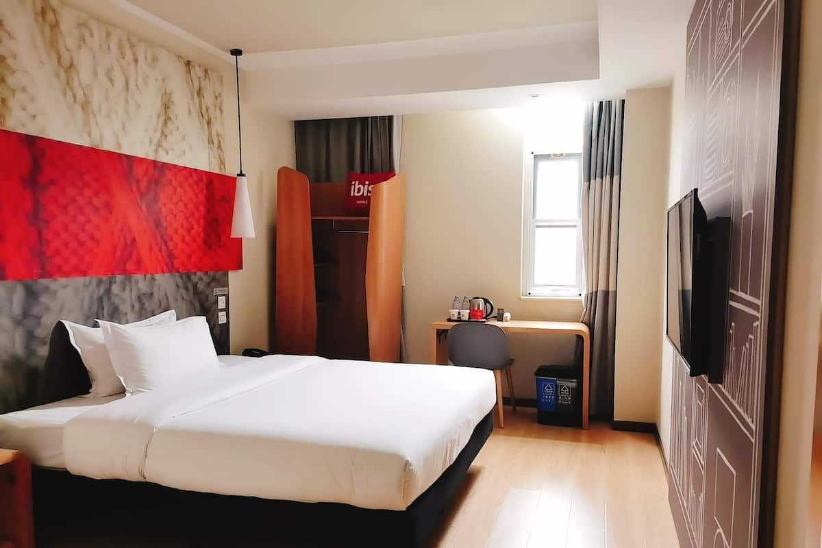 Een hotelkamer met een bed, een bureau met stoel, een kledingkast, een televisie en een raam met gordijnen.