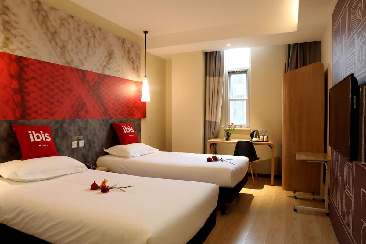 Een hotelkamer met twee bedden, een bureau, een televisie en een groot raam.