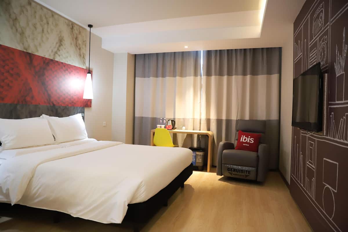 Een hotelkamer met een bed, een bureau, een stoel, een televisie en een muur met een muurschildering.
